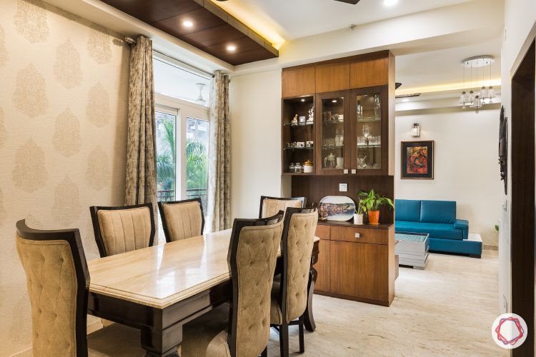 Livspace noida-wooden ceiling-beige wallpaper-golden motifs-marble topped table-wooden crockery unit