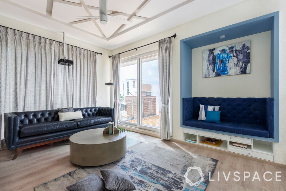 villa house design-blue sofa-niche seating-pop false ceiling-extended flooring-projector-bookshelf