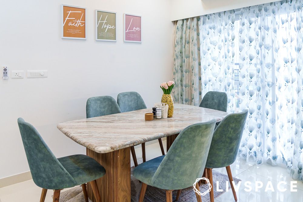 A marble dining table design with wooden legs and plush sea green chairs